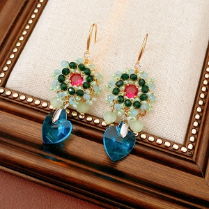 Dettaglio di orecchini a fiore con perline vintage e ciondolo a cuore in cristallo blu