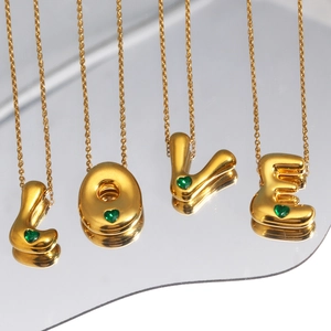 Macro detail of gold-plated puffy letter pendants LOVE with green heart gemstones