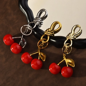 Three red cherry resin keychains with gold and silver metal clips on leather background