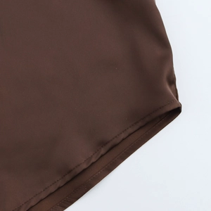 Vue détaillée de l'ourlet de la chemise brune montrant des coutures précises et le tissu