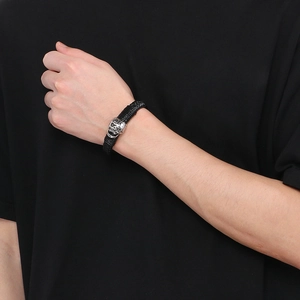 Detail shot of black braided leather bracelet with a silver skull motif for men