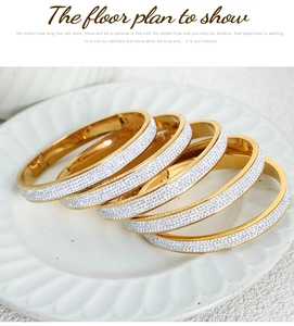 Close-up of five stacked gold-tone bangles with micro-pave crystals on a white ceramic plate