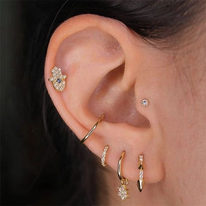 Detail of hamsa hand and diamond stud earrings set in gold on a model ear