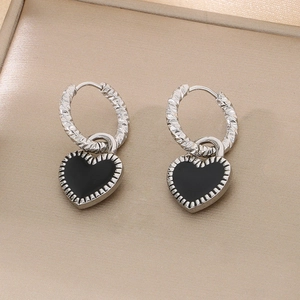 Détail de boucles d'oreilles cœur avec émail noir et finition argentée texturée