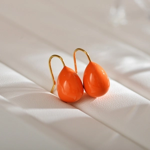 Detail of glossy orange teardrop earrings with elegant golden hooks on white texture