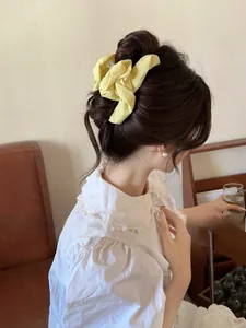 Close-up of a pale yellow pleated fabric hair claw clip styled on a model in a cozy setting