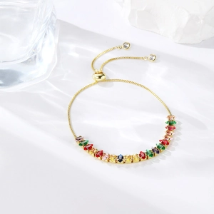Detail of adjustable gold bracelet with colorful marquise-cut zircons on a white stone background