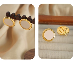 Detail view of round gold-tone earrings with cream enamel on a wooden display stand