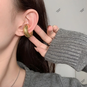 Close-up of a bold gold-plated hollow cuff earring on a model's ear cartilage