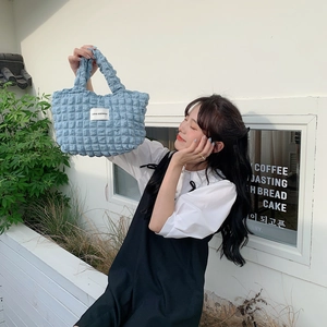 Detail of light blue bubble textured tote bag carried by a model in a cafe setting