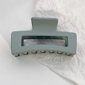 Detail view of large matte grey-green rectangular hair claw clip with cutout design