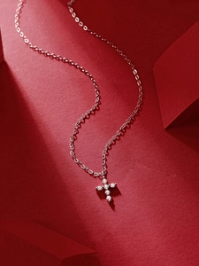 Detailed view of silver cross necklace with round clear stones on a red artistic background