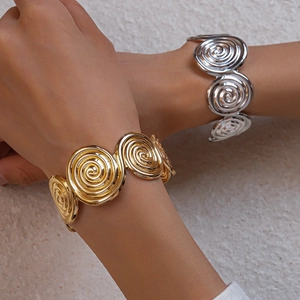 Close-up of golden and silver textured spiral geometric open bangles on a wrist