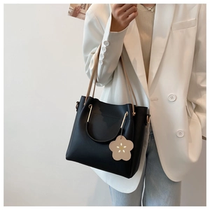 Detail der schwarzen Beuteltasche mit beigen Riemen und Blumenanhänger auf weißem Blazer