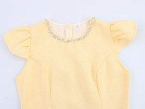 Dettaglio del vestito in tweed giallo con scollo in strass e maniche a volant