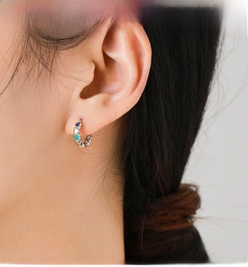 Close-up of a woman wearing colorful enamel heart-shaped silver hoop earrings