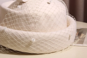 Detail of elegant cream wool pillbox hat featuring vintage mesh veil with white pom-poms