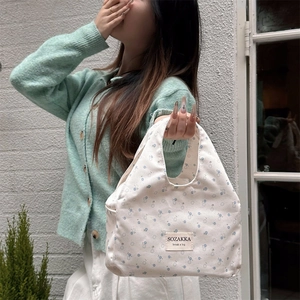 Outdoor shot of a canvas lunch bag with light blue floral print and integrated handle