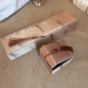 Macro shot of two elegant silk-textured jewelry boxes featuring luxury brown tassels