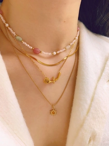 Close-up of layered gold snake chain with floral pendants and colorful beads