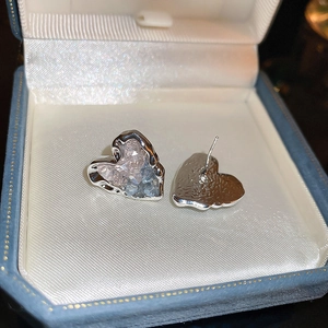 Macro detail of silver heart stud earrings with pink and blue crystal inlay in a jewelry box