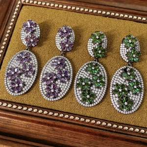 Macro detail of vintage oval earrings with zircon floral patterns in purple and green