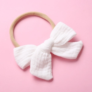 Close-up of white cotton muslin bow with beige elastic nylon headband for babies
