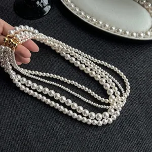 Detailed view of multilayer pearl necklace with gold sphere clasp on dark grey fabric