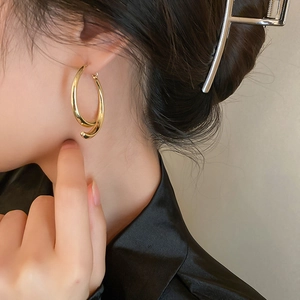 Close-up of a model wearing a glossy twisted golden double-hoop earring in metal finish