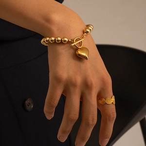 Golden bead bracelet with heart pendant and spiral textured ring on model wrist