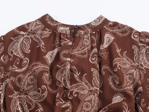Dettaglio dello scollo rotondo con motivo paisley e bottoni neri sull'abito marrone