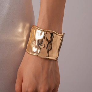 Vue rapprochée du large bracelet doré à bords ondulés et finition miroir haute brillance