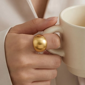 Macro shot of a wide gold stainless steel dome ring worn by a model holding a cup