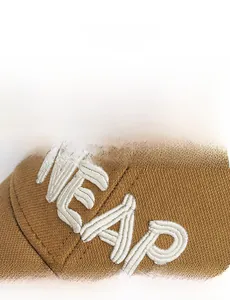 Detailed view of white 3D embroidery NEAR on brown distressed cotton baseball cap