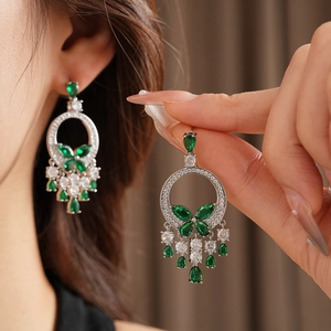 Vue détaillée des boucles d'oreilles papillon avec pierres vert émeraude et blanches sur modèle