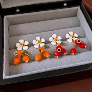 Detail of gold-plated flower earrings with enamel persimmon and pomegranate charms