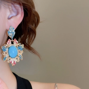 Detailed close-up of retro enamel earrings with turquoise stones on model's ear