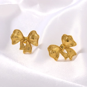 Elegant gold bow earrings on white silk fabric, minimalist and fashionable jewelry for women