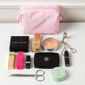 Detail of a pink pleated makeup bag surrounded by various cosmetic products on a white desk.