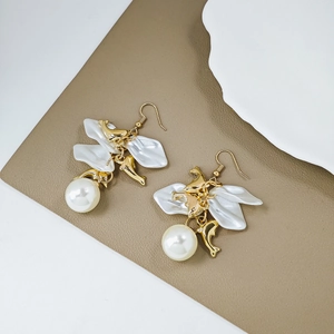 Detailed view of gold dolphin earrings with white petals and large pearls on a leather backdrop