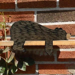 Rustic carved wooden brown bear door stopper resting on a shelf near a brick wall