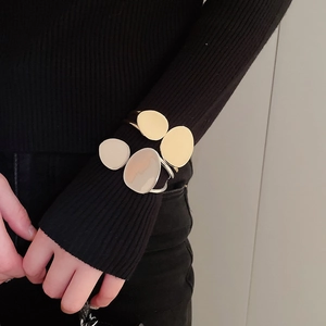 Detail of stacked irregular oval bracelets in gold and beige enamel on a black sleeve