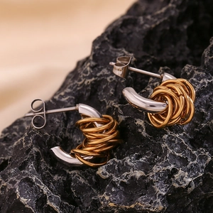 Detailed view of bicolor silver and gold twisted C-shape metal hoop earrings on a black rock
