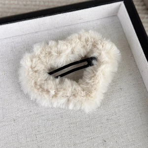 Detail of beige plush heart-shaped hair clip with black metal snap fastener on a tray
