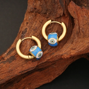 Golden evil eye hoop earrings with blue and white enamel beads on a dark wood background