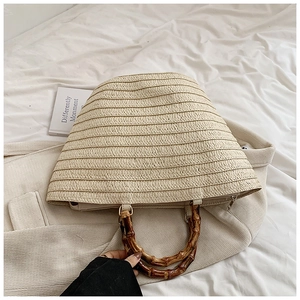 Detail of hand-woven straw tote bag featuring vintage bamboo handles and metal rings