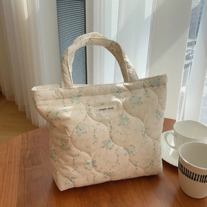 Sac à main matelassé à fleurs avec étiquette tissée posé sur une table en bois