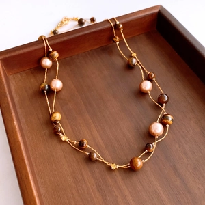 Detail of vintage tiger eye and pearl double-layer necklace on a wooden tray