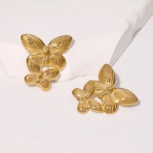 Vintage gold butterfly stud earrings with layered wings on a textured white stone