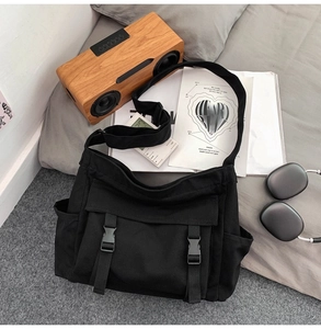 Vue de dessus d'un sac bandoulière en toile noire avec deux poches à boucle sur fond gris